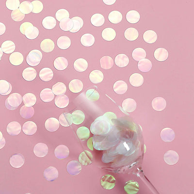 Iridescent confetti circles scattered beside a clear glass on a pink background.