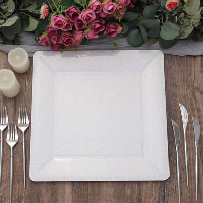 Elegant square dinner plate with floral design, surrounded by cutlery and decorations.