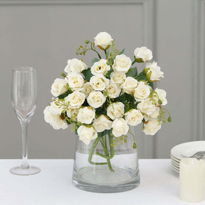 White rose bouquet in a clear vase with glassware and plates in the background.