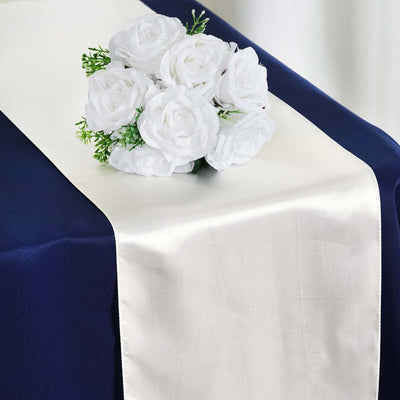White satin table runner with artificial rose bouquet on a navy tablecloth.
