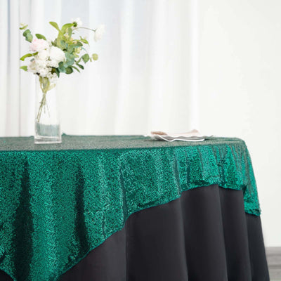 Green sequin tablecloth draping over a black table with a vase of flowers.