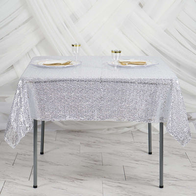 Silver sequin tablecloth draped over a table with plates and glasses.