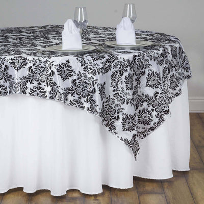 Black and white damask tablecloth draped over a round table with glasses and napkins.