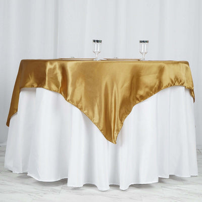 Gold satin table cover draped over a round table with white linen underneath.
