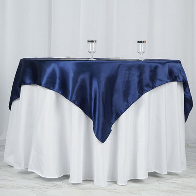Navy satin tablecloth draped over a white table with glass candle holders