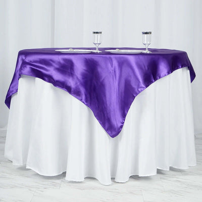 Purple satin tablecloth draped over a round table with white skirt.