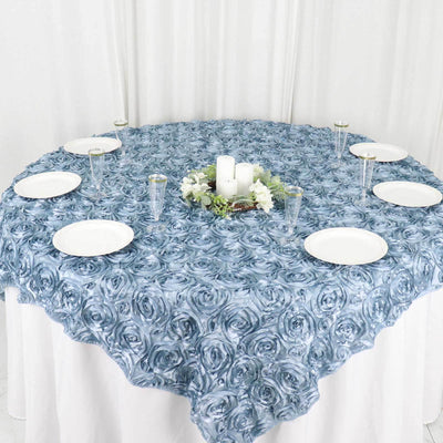 Blue rose-patterned tablecloth with white plates and candles arranged around it.