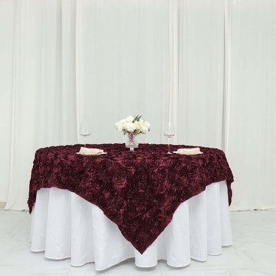 Burgundy rose-patterned tablecloth draped over a white table with floral centerpiece.