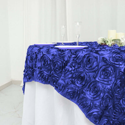 Royal blue rose tablecloth on a white table with glassware and candles.