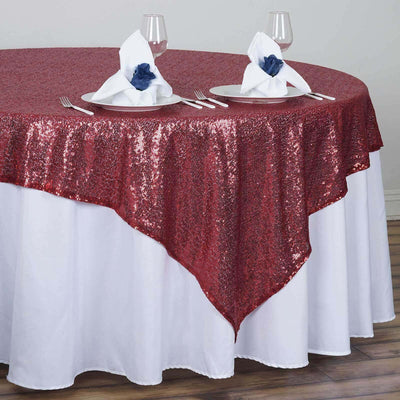 Red sequin tablecloth draped elegantly over a round table setting with napkins.