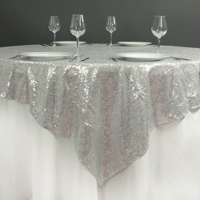 Silver sequined tablecloth with plates and glasses set for dining.