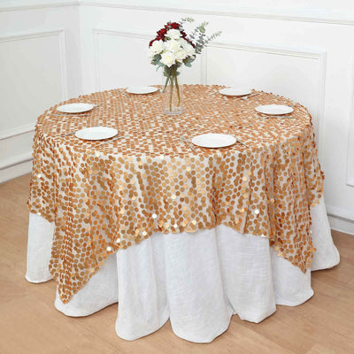 Round gold sequin tablecloth on a dining table with white plates and floral centerpiece.