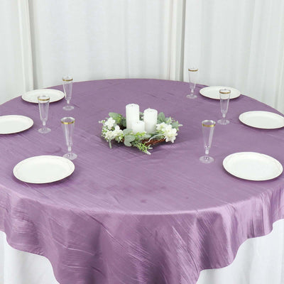 Elegant round table set with purple cloth, candles, and glassware.