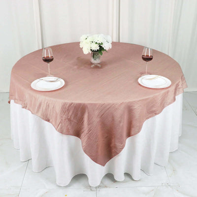 Round table set with a blush pink tablecloth, wine glasses, and white plates.