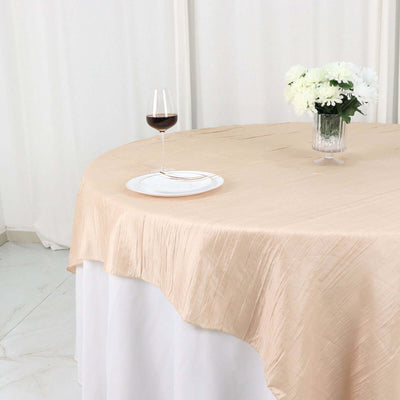Elegant beige tablecloth draped over a round table with a glass of wine and flowers.