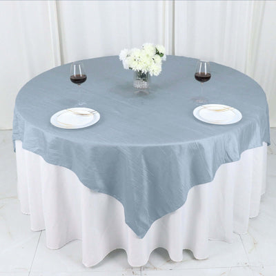 Round blue tablecloth draped over a table set with plates and glasses.
