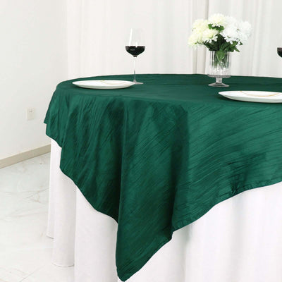 Green tablecloth draped over a round table with wine glasses and floral centerpiece.