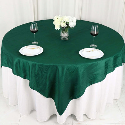Elegant green tablecloth on a round table with white skirt, wine glasses, and plates.