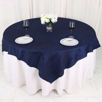 Navy tablecloth draped over a round table with wine glasses and floral centerpiece.