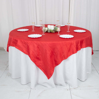 Red tablecloth draped over a round table with plates and candles.