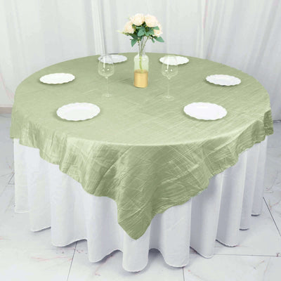 Round olive green tablecloth draped over a round table with plates and glasses.