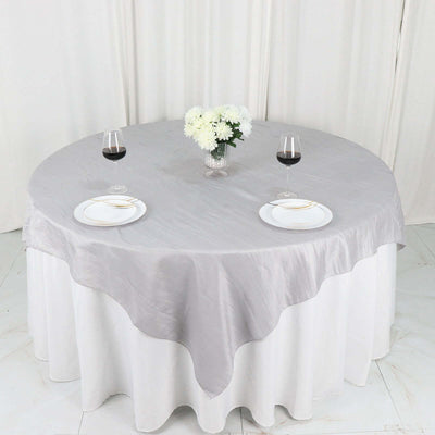 Round silver tablecloth on a dining table set with wine glasses and plates.