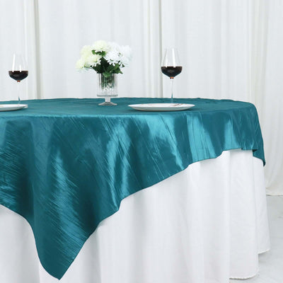 Teal satin tablecloth draped over a white table with wine glasses and flowers.