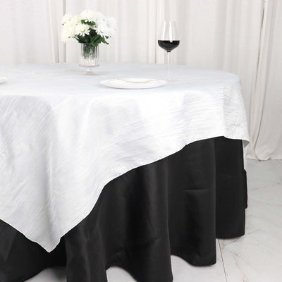 Elegant white and black tablecloth draped over a table with floral centerpiece and wine glass.