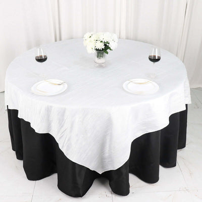 Round table set with a white and black tablecloth, plates, and wine glasses.