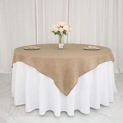 Round burlap tablecloth draped over a white table, set with plates and flowers.