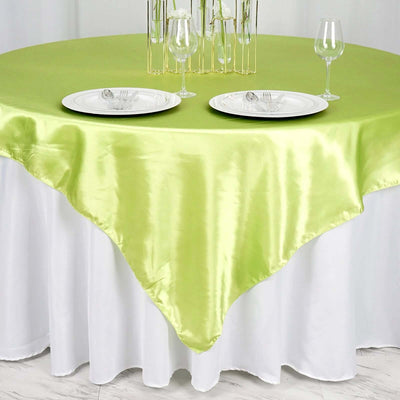 Green satin tablecloth draped over a round table with plates and glasses.