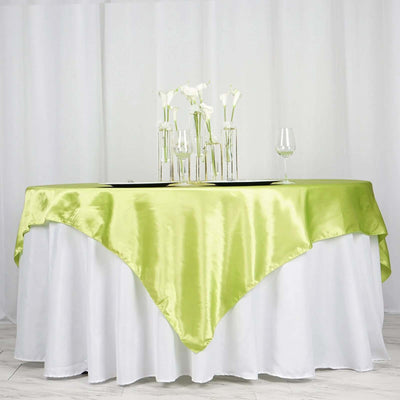 Green satin tablecloth draped over a white table with decorative vases and glassware.