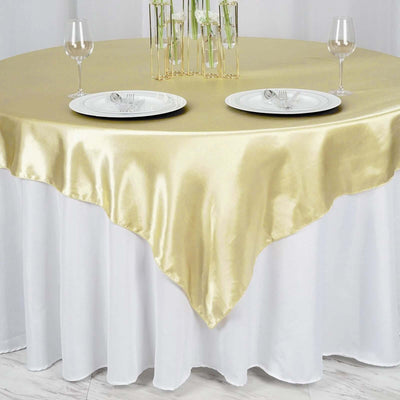 Gold satin tablecloth draped over a round table set with plates and glasses.
