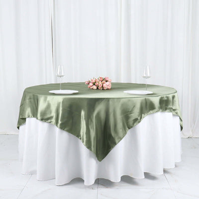 Elegant green satin tablecloth draped over a round table with plates and glasses.