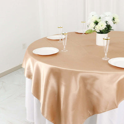 Elegant gold satin tablecloth draped on round table with plates and glasses.