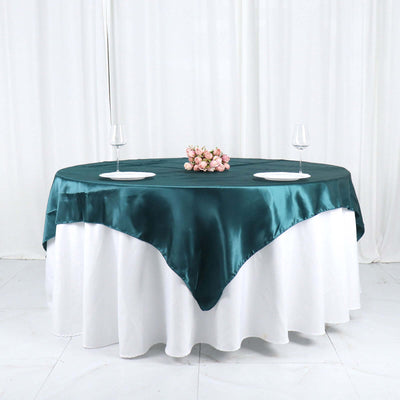 Teal satin tablecloth draped elegantly over a round dining table with floral centerpiece.