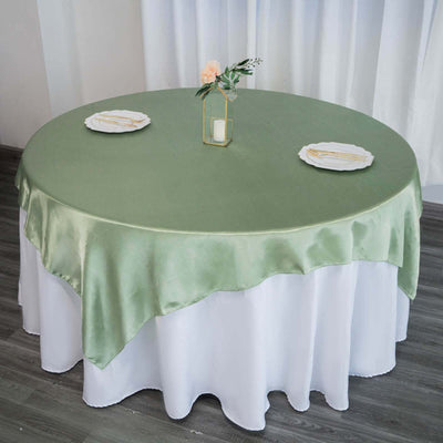 Round table dressed with a green satin tablecloth and elegant dinnerware.