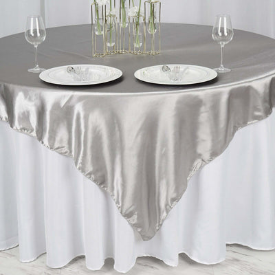 Elegant silver tablecloth on a round table set for two with glassware and plates.
