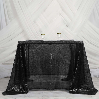Black sequin tablecloth on a table with glasses, styled against draped white fabric.