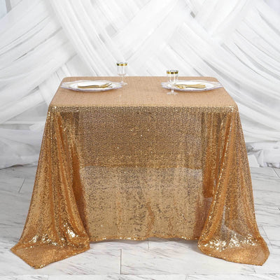 Gold sequin tablecloth on a decorated table with plates and glasses.