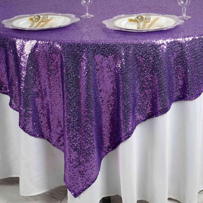 Purple sequin tablecloth draping over a white table with plates and cutlery set.