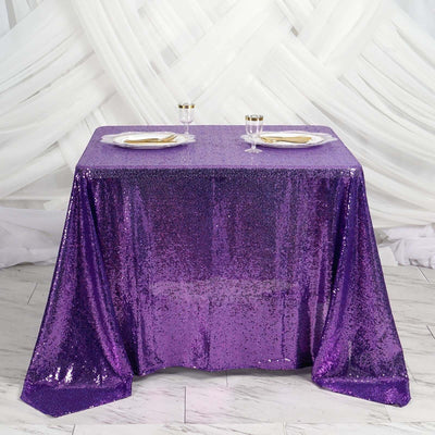 Purple sequin tablecloth draped on a table with gold plates and glasses.