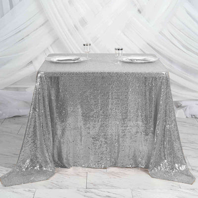 Silver sequin tablecloth on a table set for two with glasses and plates.