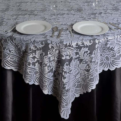 White lace tablecloth draped elegantly on a dark table with plates and cutlery.