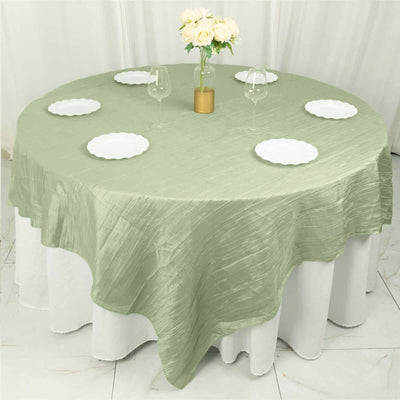 Round olive green tablecloth on a dining table with plates and glasses.