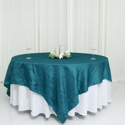 Teal tablecloth draped over a round table with decorative centerpiece and glasses.