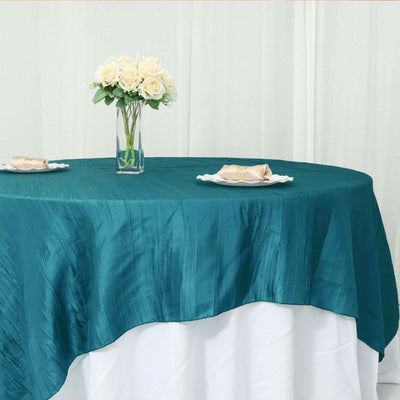 Teal tablecloth draped over a table with a vase of flowers and tableware.