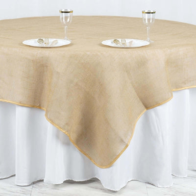 Round burlap tablecloth with gold trim on a white table.