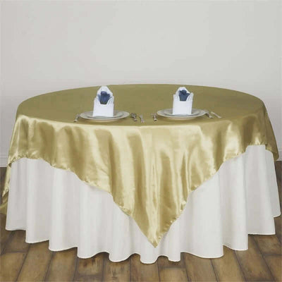 Gold satin tablecloth draped over a round table set with plates and napkins.