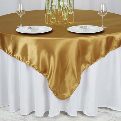Gold satin tablecloth draped over a white table with dinner plates and glasses.